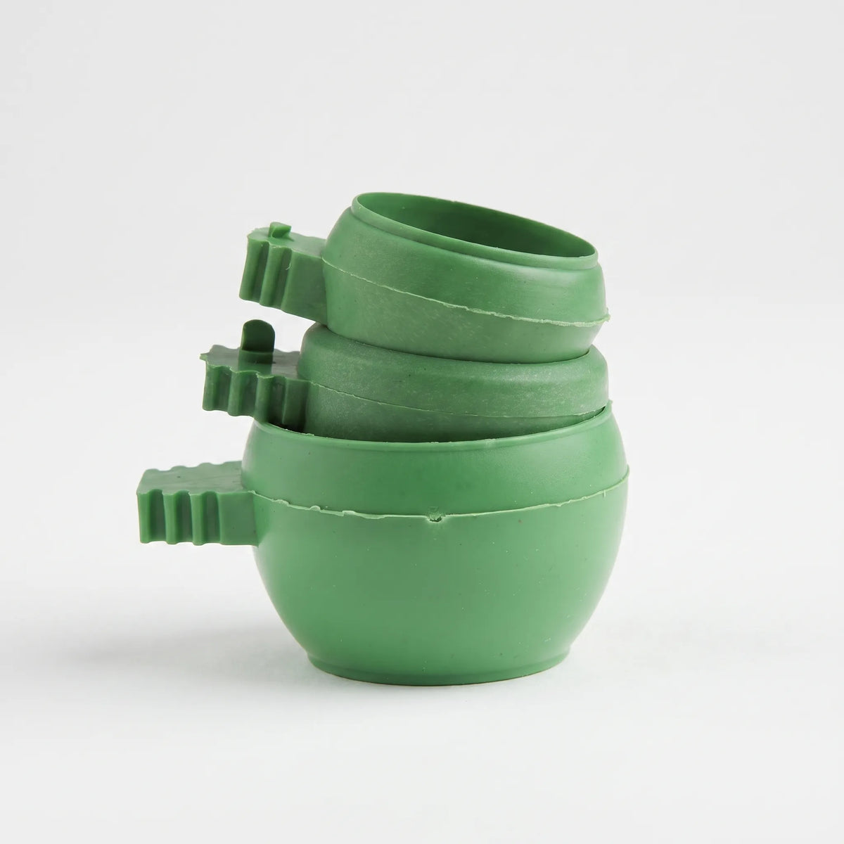 Three green plastic bowls with ridged clip handles stacked inside one another on a plain white background. 1