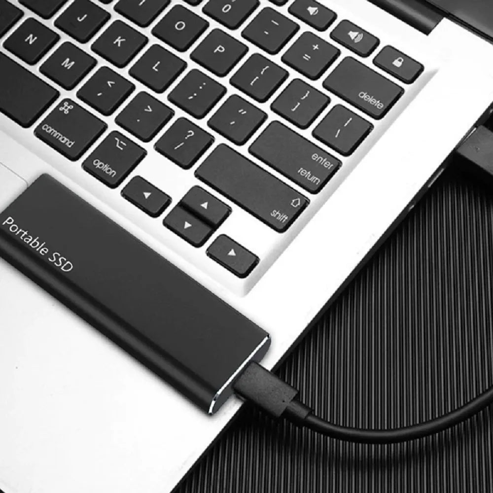 Black drive resting on a laptop keyboard, connected by a black cable plugged into its USB-C port. 5