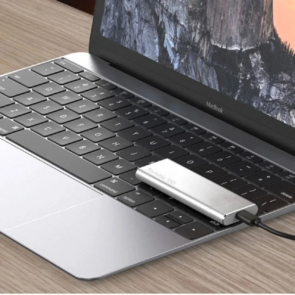 Silver drive lying on the keys of a slim laptop on a wooden desk, with a black cable attached. 7