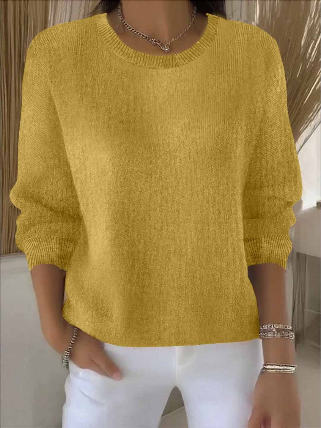 Model wears the round-neck knit jumper in mustard yellow with white trousers, bracelets and a chain necklace 8