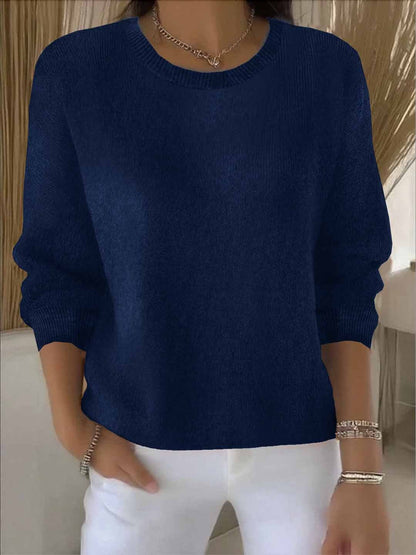 Model wears the round-neck knit jumper in navy blue with white trousers, bracelets and a chain necklace 9