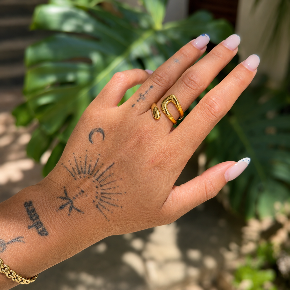 Ring worn on a tattooed hand outdoors, the open gold band sitting on the middle finger 3
