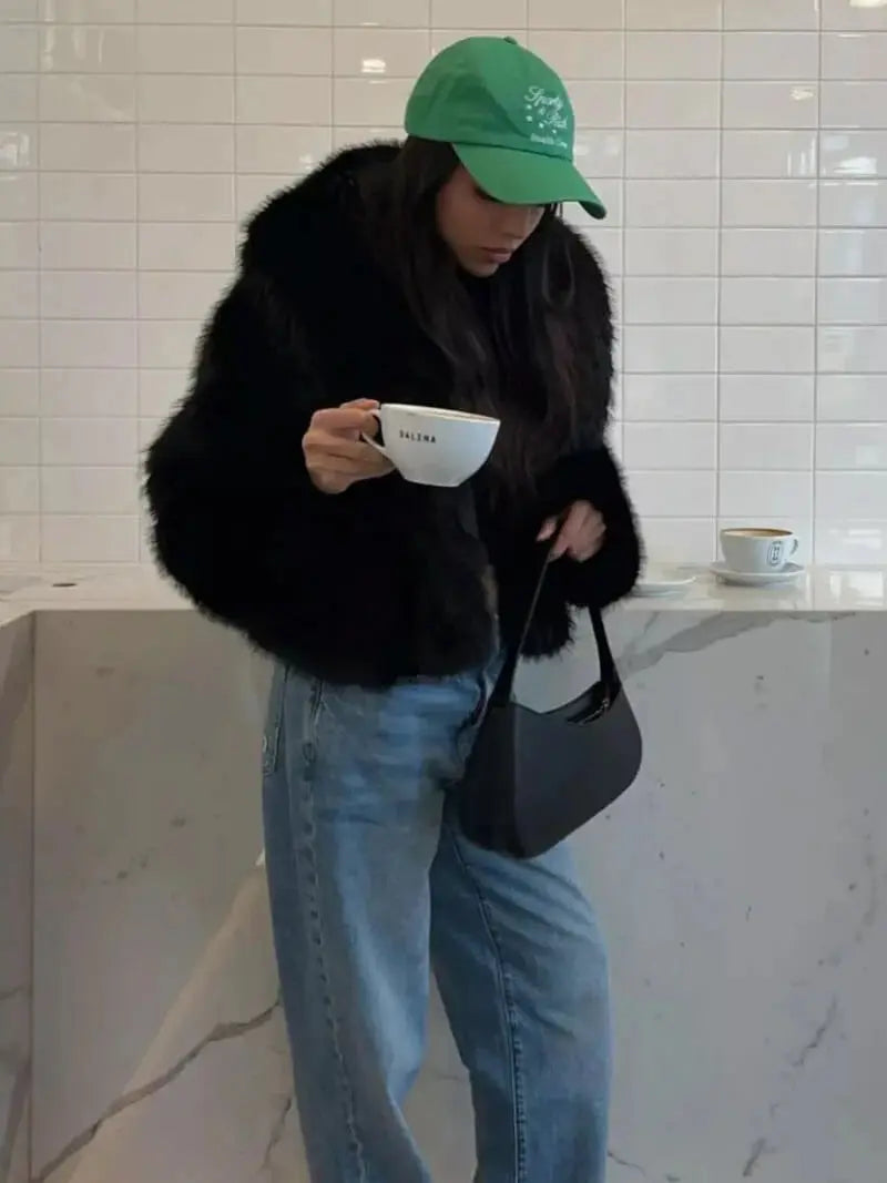 Woman in a green cap and jeans wearing the black faux fur coat while holding a coffee cup 10