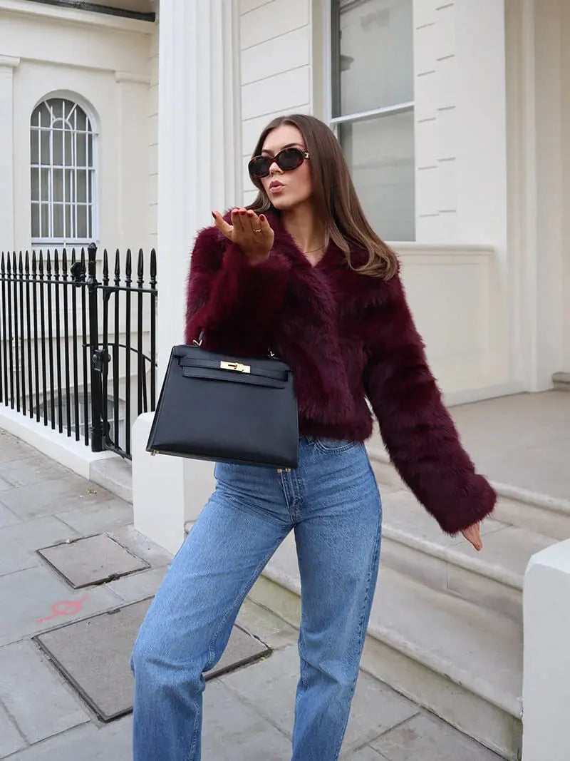 Woman in the burgundy faux fur coat with blue jeans, holding a black handbag and blowing a kiss 12