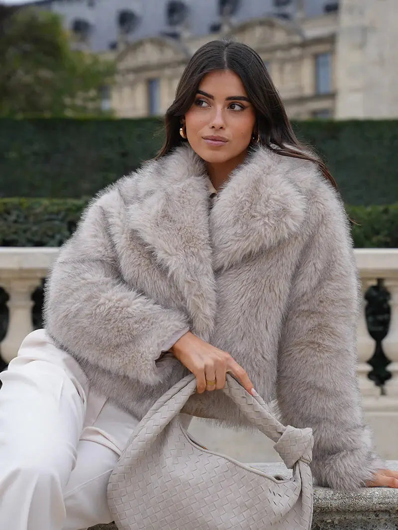 Woman in a light grey faux fur coat with a big collar, holding a woven bag 6