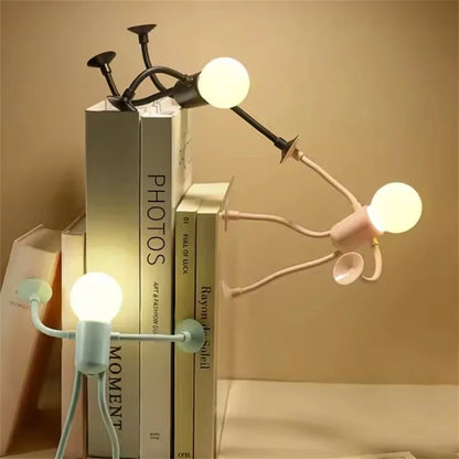 Three glowing figure lights in black, pink and pale green posed on a stack of books 1