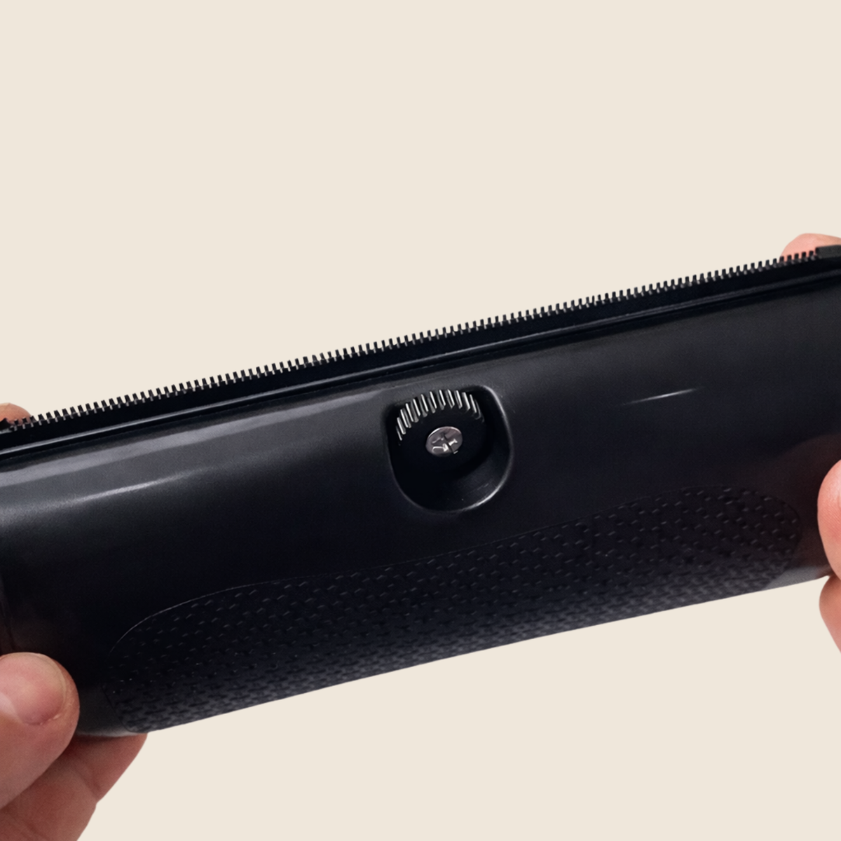 Close-up of the brush's fine toothed edge and the small adjustment screw set into the glossy black body, held in one hand. 4