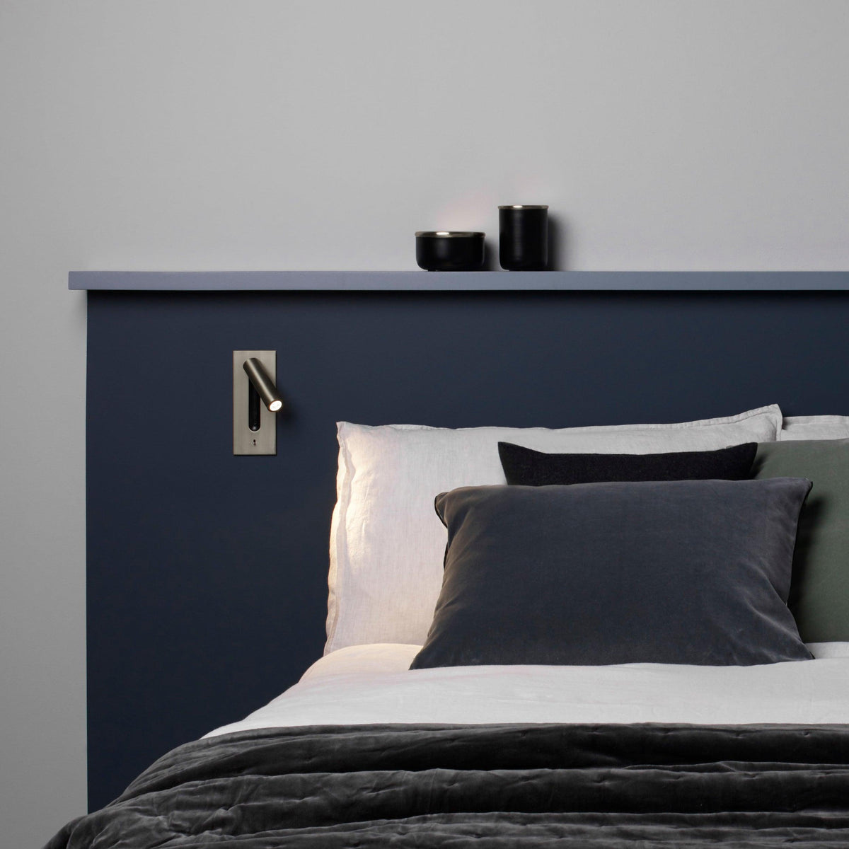Bronze wall light fitted on a navy headboard panel above grey and white bedding 30