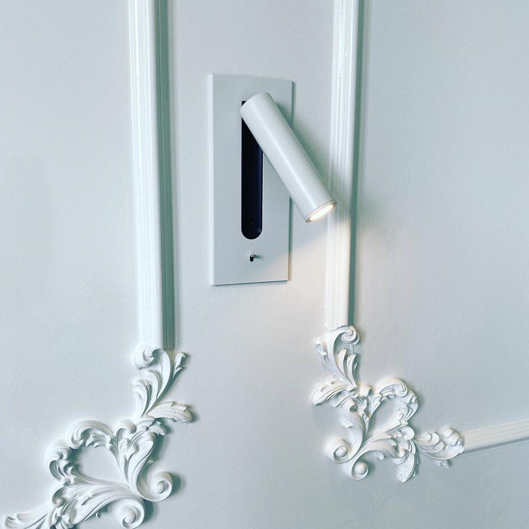 White wall light switched on, mounted on a white panelled wall with ornate plaster scrollwork 27