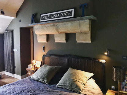 Lit wall light on a dark green bedroom wall beside a cane headboard and bedside lamp 37