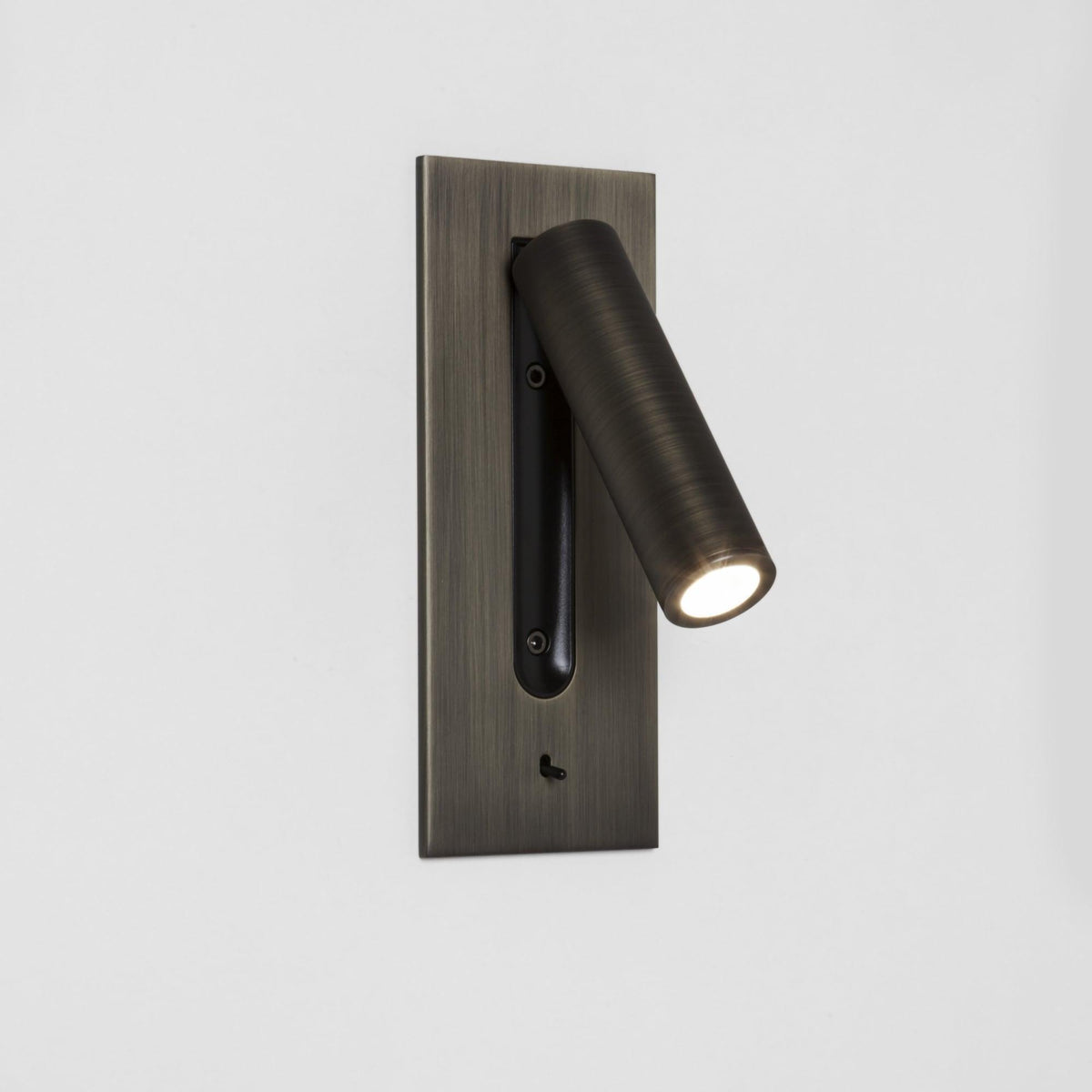 Champagne-gold wall light with lit tube angled left, black recess behind it and toggle switch below 17