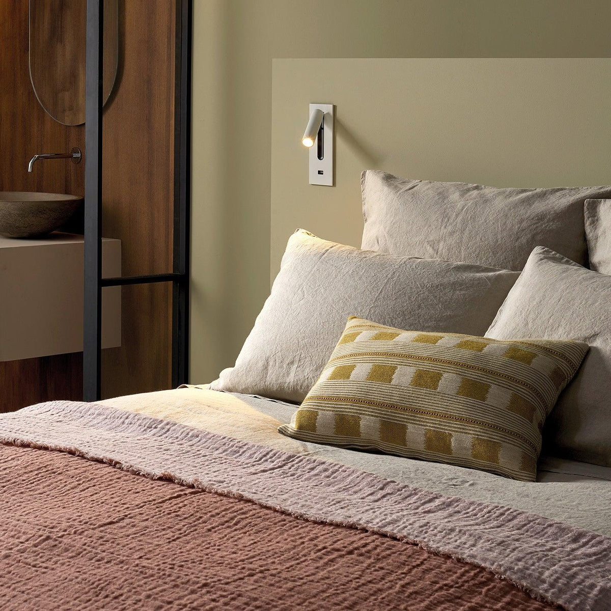 White wall light with a built-in charging port below, mounted above a bed with linen bedding 31