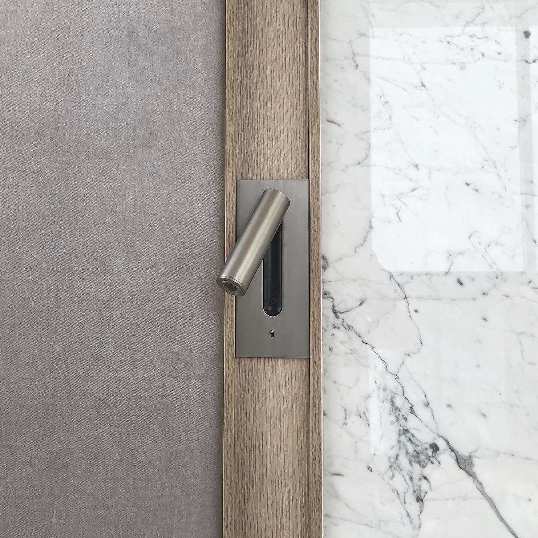 Nickel finish wall light set into a wooden strip between grey fabric and white marble 33