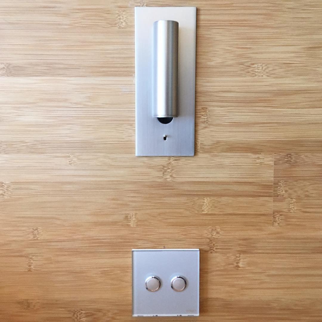Silver wall light with the tube folded upright against its plate, above a two-button switch on bamboo 34