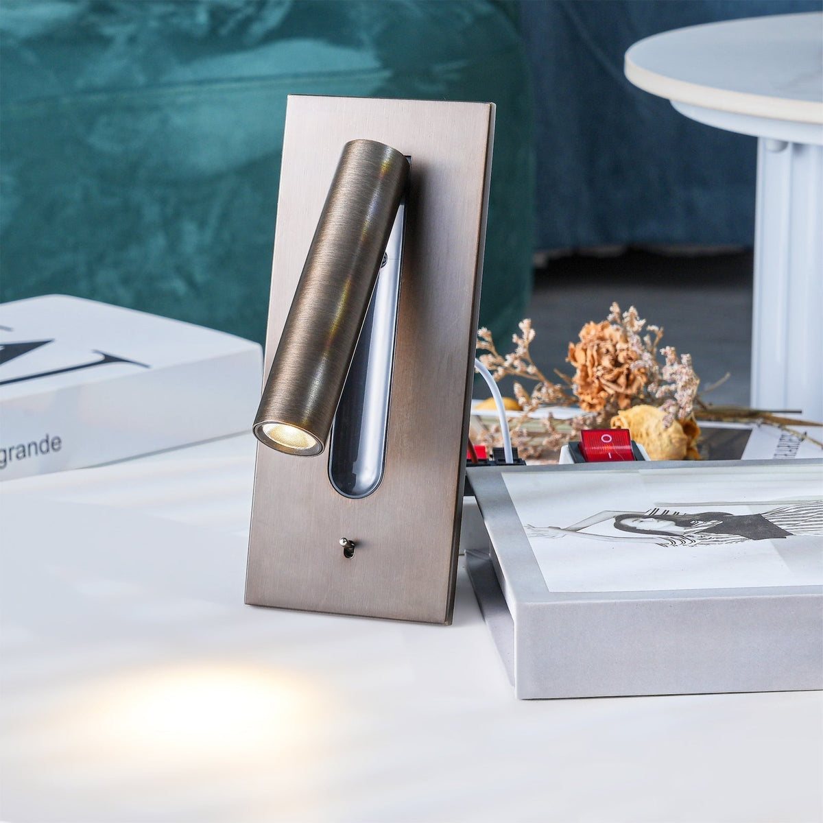 Bronze wall light standing on a table among books and dried flowers, casting a warm glow 28