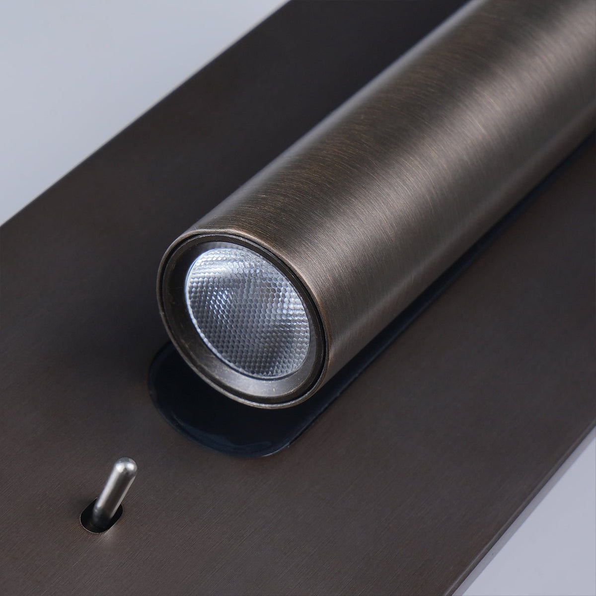 Bronze wall light on a white wall, lit tube angled right with the black recess visible 18
