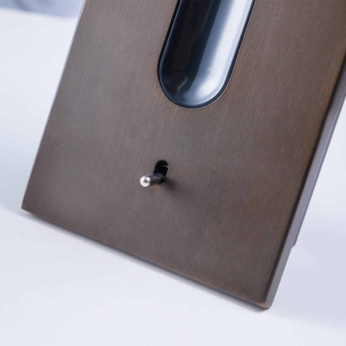 Close-up of the bronze tube's LED lens with a textured diffuser, and the toggle switch beside it 19