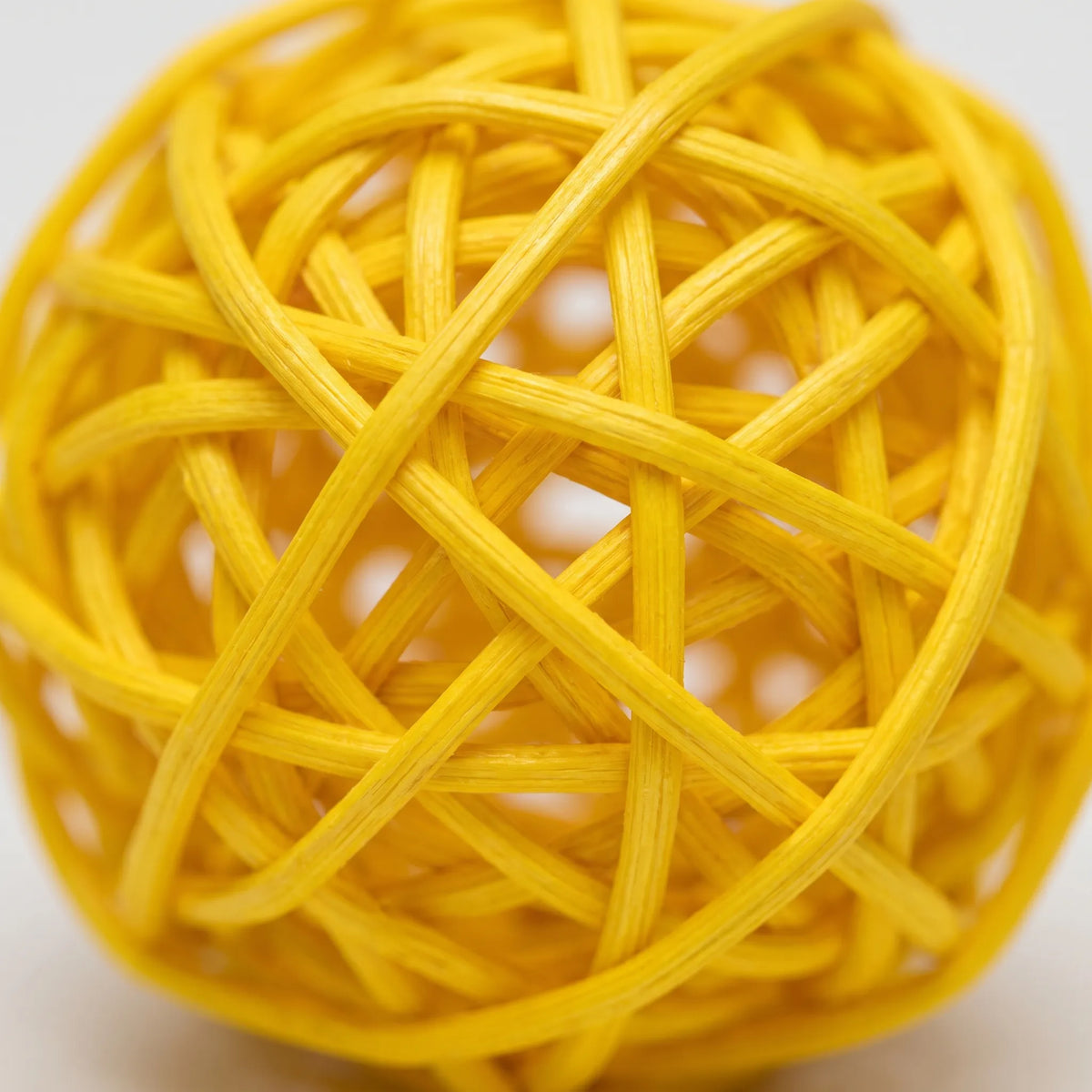 Close-up of a yellow woven ball showing the interlaced strands of cane and the open gaps between them. 4