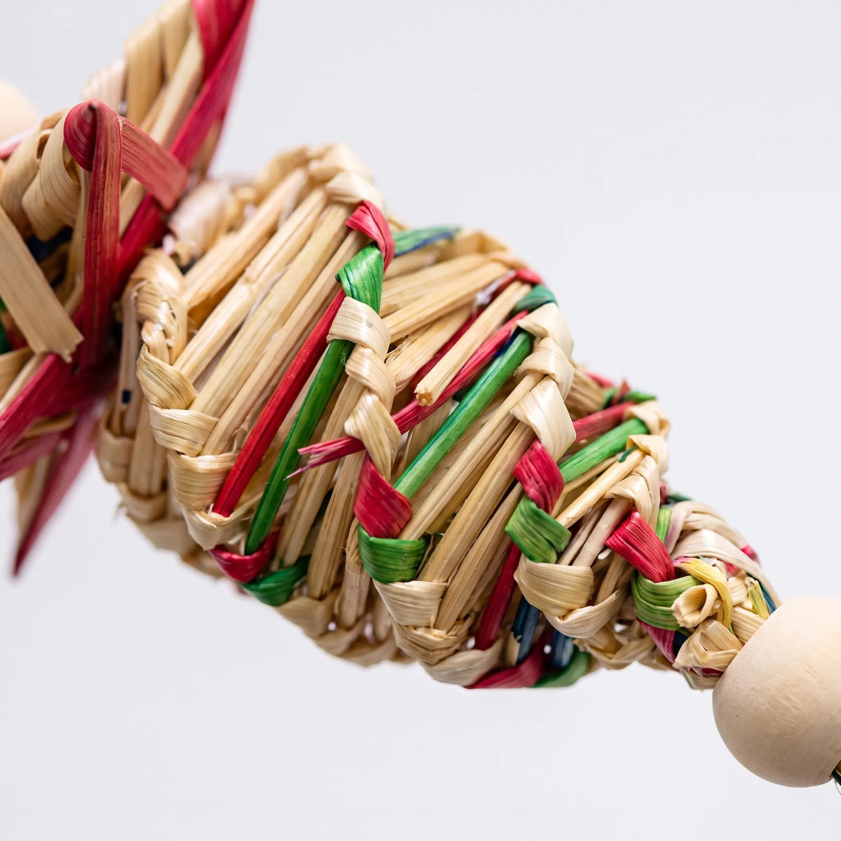 Close-up of the braided straw weave in red, green and natural strands, with a smooth wooden bead at the end. 3