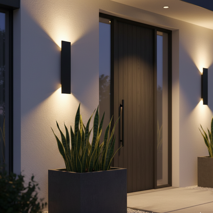 Two black wall lights casting warm up-and-down light on a white rendered wall beside a dark front door and planters. 2