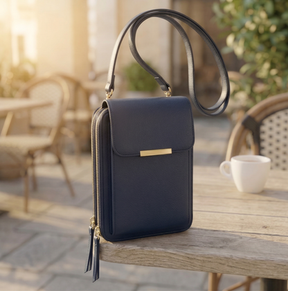 Navy blue version of the flap crossbody bag with gold bar clasp and double zips, placed on a wooden cafe table. 3