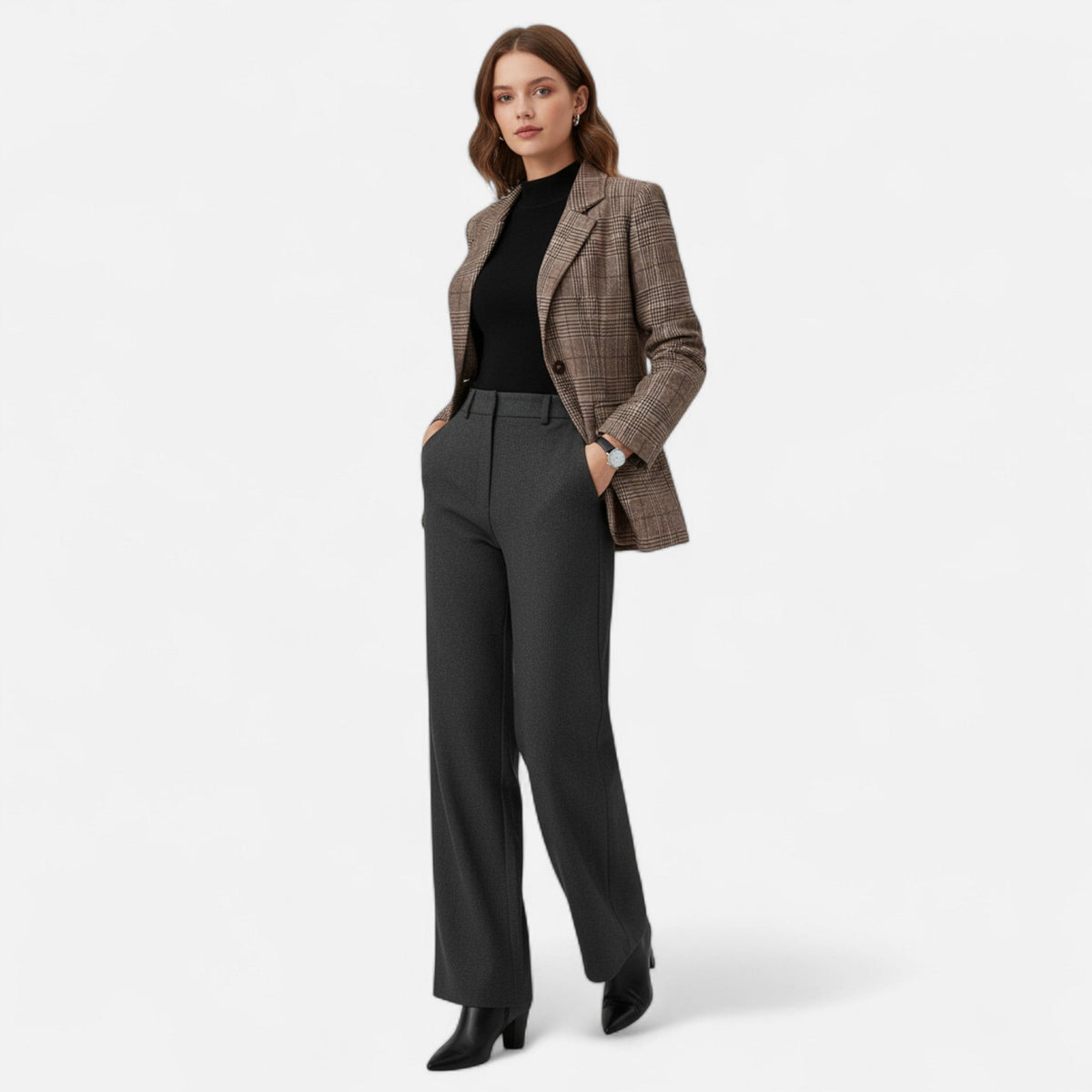 Full-length shot of a model wearing the brown check blazer over a black top with grey trousers and black ankle boots. 2