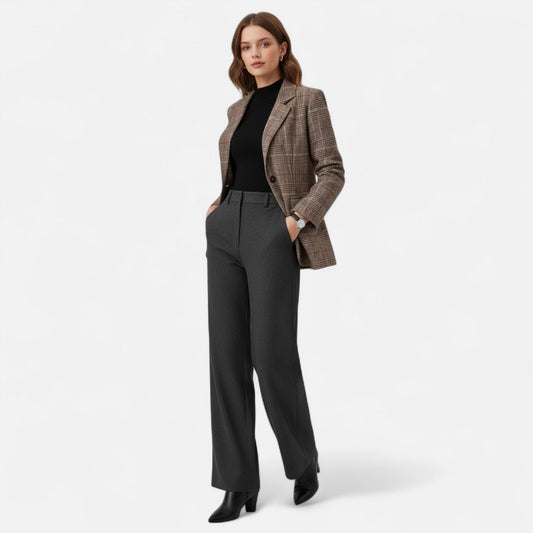 Full-length shot of a model wearing the brown check blazer over a black top with grey trousers and black ankle boots. 2