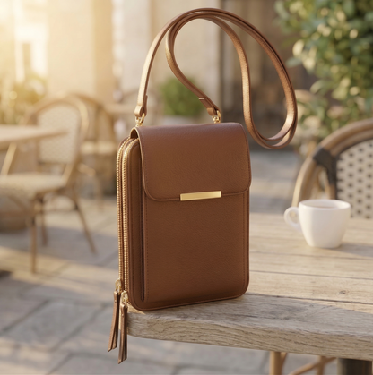 Tan brown version of the flap crossbody bag with gold bar clasp and slim strap, resting on a weathered outdoor table. 4