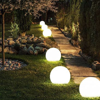 Evening garden path edged with glowing spheres of varying sizes on the grass, stretching away between rockery stones and tall hedges. 6