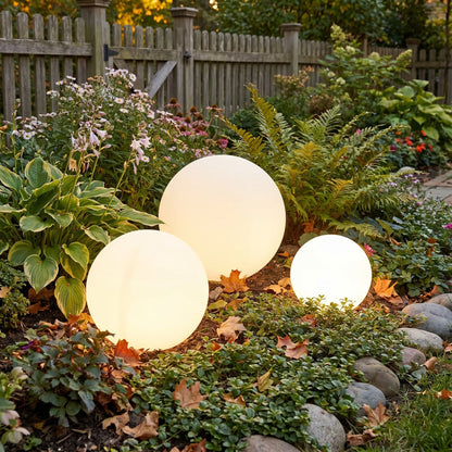 Three illuminated spheres of different sizes set in a flower bed beside a wooden picket fence, surrounded by autumn leaves. 2