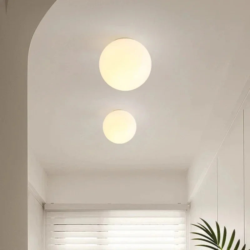 Two ceiling-mounted opal glass spheres of different sizes glowing warmly in a white, arched corridor 7