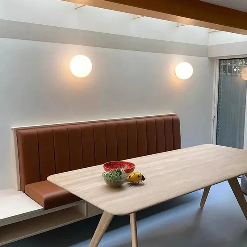 Two lit glass spheres on a white wall above a leather banquette and wooden dining table 12