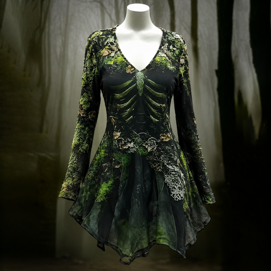 Front view on a mannequin of a V-neck, long-sleeved dress with a rib cage and moss print and a pointed, uneven hem, against a misty forest backdrop. 1