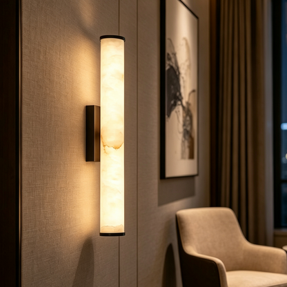 Close view of a glowing marble wall light on a textured fabric wall, beside framed abstract art and a cream armchair. 12