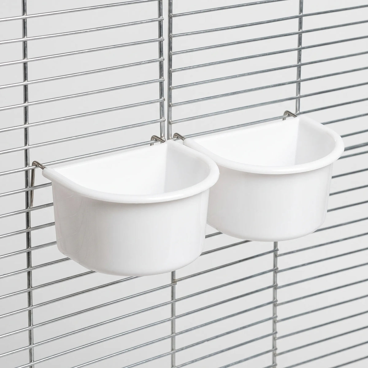 Two white half-round bowls hanging on a cage grille, held in place by thin metal wire hangers. 7