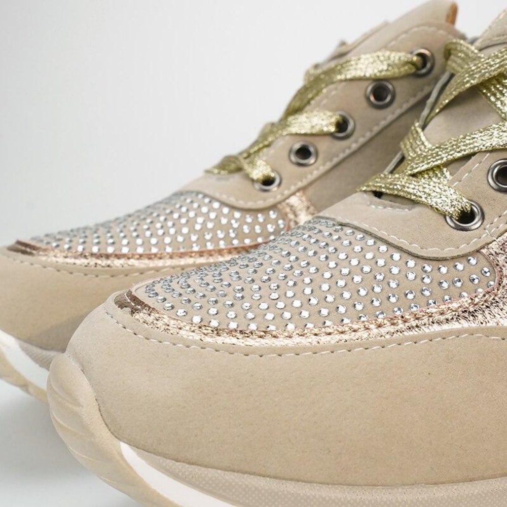 Close-up of the toe area of a pair of beige trainers, showing crystal-studded panels, gold laces and a white sole. 10