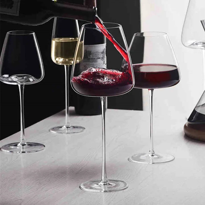 Red wine being poured into a tall glass, with white wine and red glasses on a pale table 2