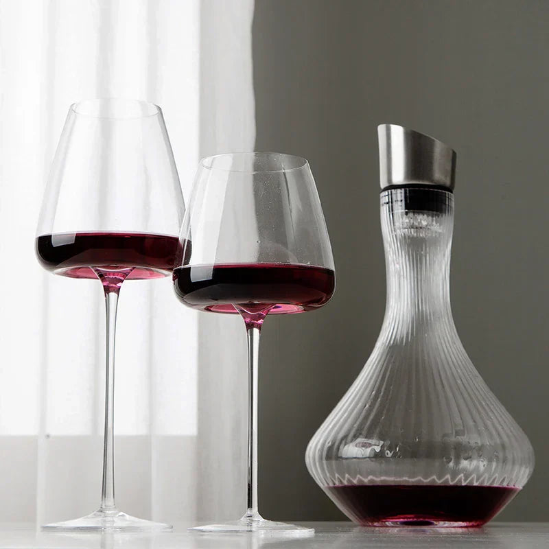 Two glasses of red wine beside a ribbed glass decanter with a metal stopper, in soft daylight 3