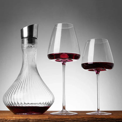 Two red wine glasses next to a ribbed decanter with a metal top, on a wooden surface 4
