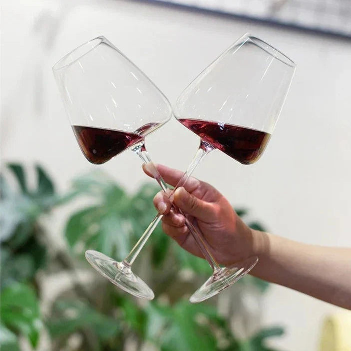 Hand holding two tilted glasses of red wine together in a toast, with green plants behind 7