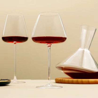 Two red wine glasses on a cream backdrop beside an angular decanter on a wooden coaster 8