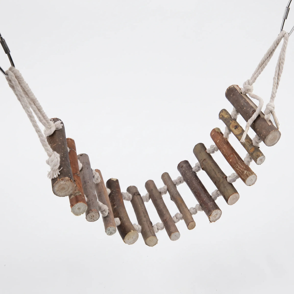 Rustic rope bridge with natural wooden twig rungs knotted onto cream cotton rope, sagging in a curve with metal clips at both ends. 1