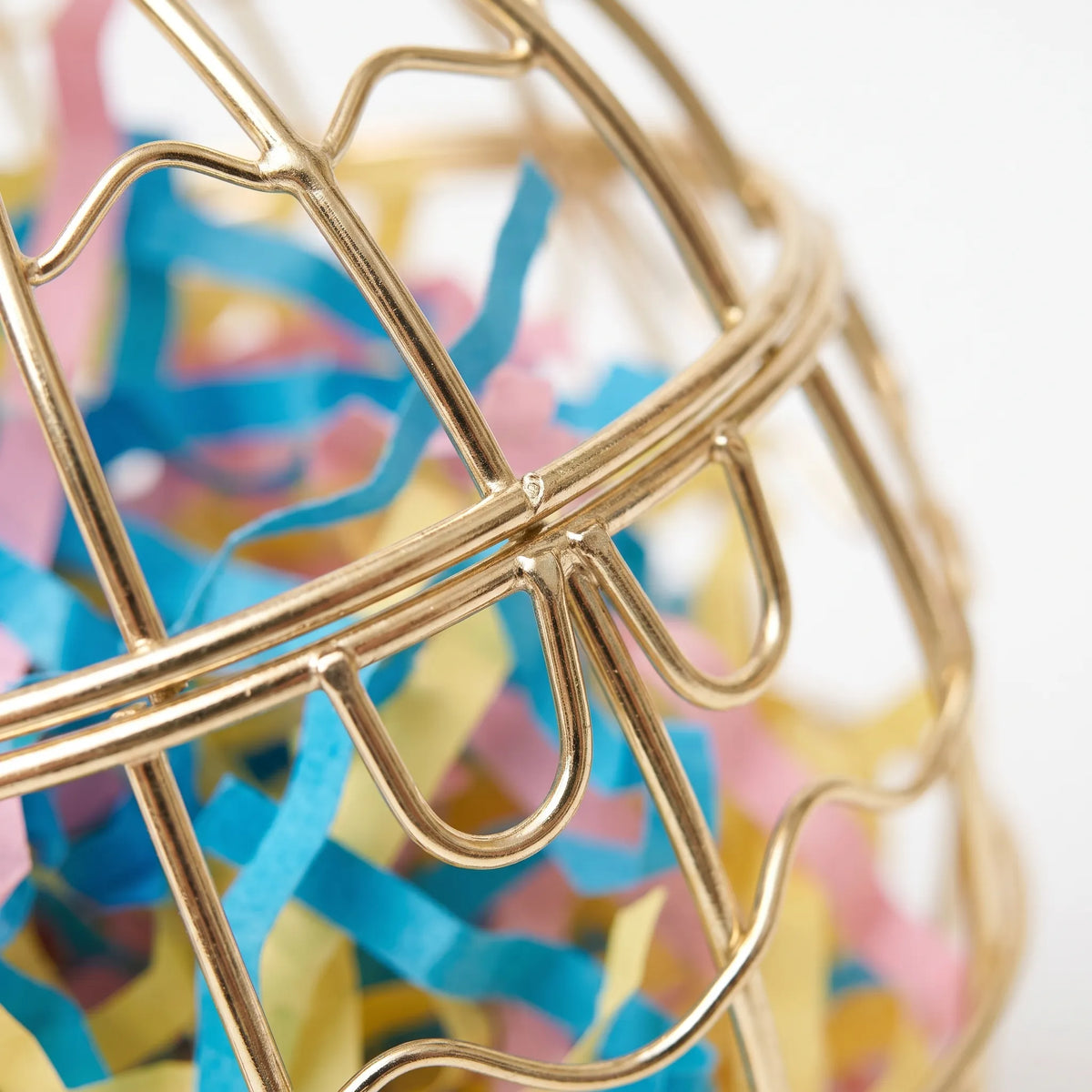 Close-up of the gold wire bars and latch loops, with blue, pink and yellow shredded paper visible inside the cage. 3