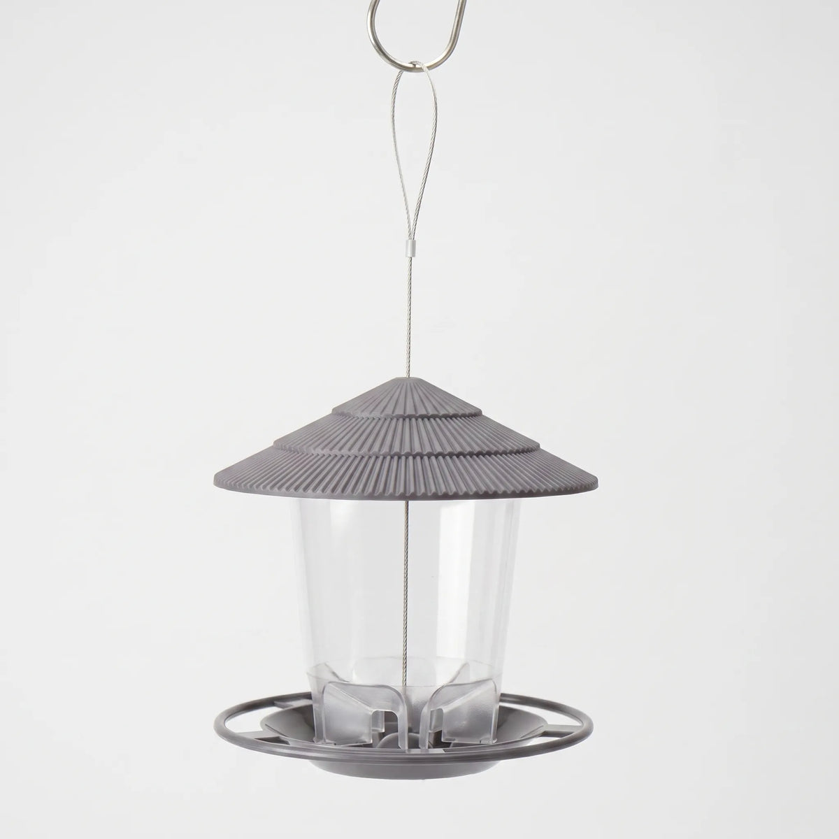 Grey hanging feeder with a ridged tiered roof, clear seed tube and round perch tray, hung from a wire loop on a hook. 1