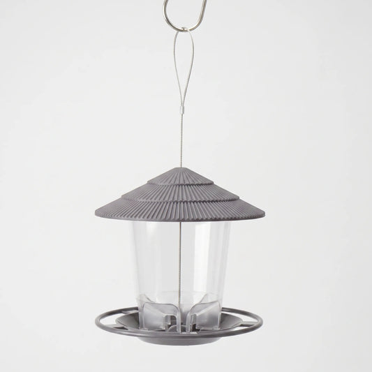 Grey hanging feeder with a ridged tiered roof, clear seed tube and round perch tray, hung from a wire loop on a hook. 1