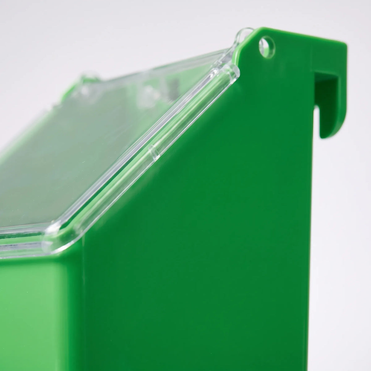 Close-up of the feeder's side edge showing the clear hinged lid, a small pivot hole and the hook that grips the cage wire. 3
