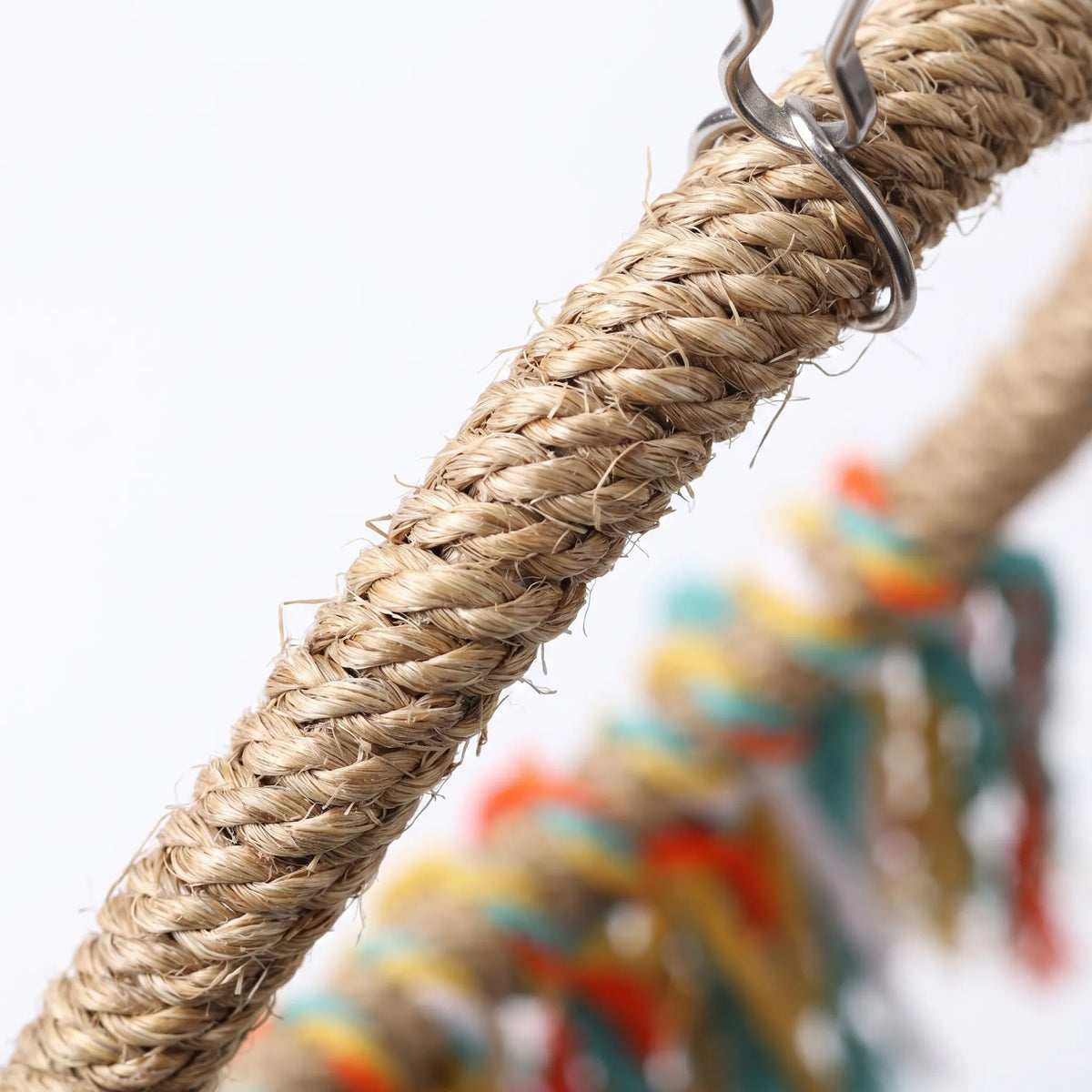 Close-up of the twisted natural fibre rope ring and the metal clip it hangs from, with the coloured tassels blurred behind. 3