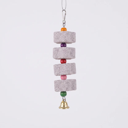 Four grey pumice blocks strung with orange, purple, red, pink and green wooden beads, a brass bell and a snap hook, on plain white. 1