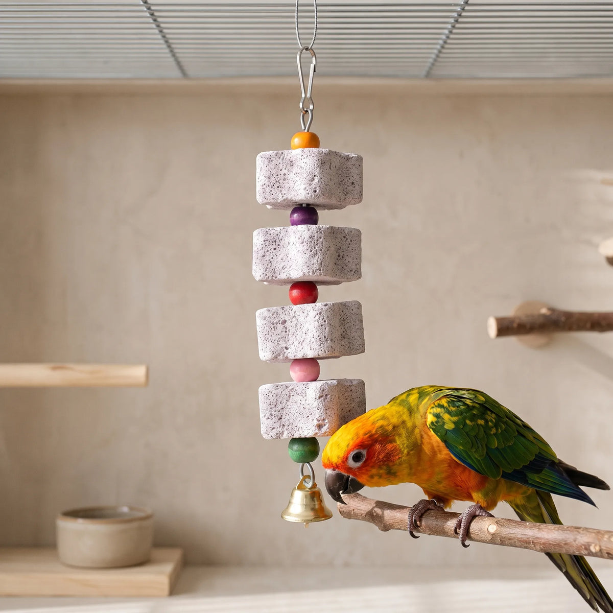 The same four-block pumice toy hanging in a cage while a sun conure perches on a branch beside it, beak close to the bottom block. 2