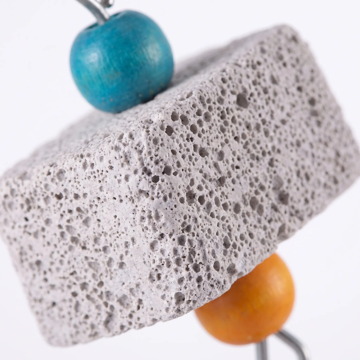Close-up of the porous, pitted texture of a grey pumice block, with a turquoise bead above and an orange bead below. 4